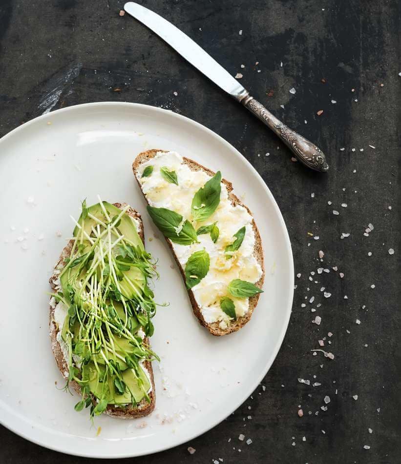 Avocado, ricotta, basil and sprout sandwiches on white ceramic plate over dark grunge backdrop, top view CATHERINE MILLER LUNCH IDEAS
